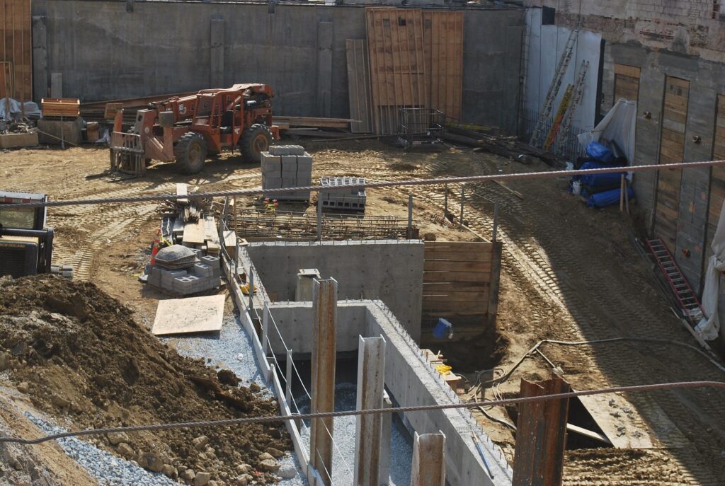 Construction site with heavy machinery, including a telehandler, stacks of concrete blocks, and excavation work, illustrating land clearing and preparation for new development projects in Detroit.